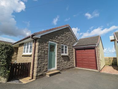 The exterior of a stone house with a green door and a red garage door under a blue sky at Island View Cottage in High Hauxley near Amble