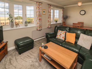 A living room with green leather sofa and ottoman wooden coffee table and dining table by the windows at Island View Cottage in High Hauxley near Amble