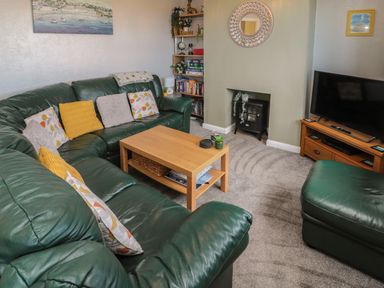 A living room with green leather sofas a wooden coffee table a fireplace and a television on a wooden stand at Island View Cottage in High Hauxley near Amble