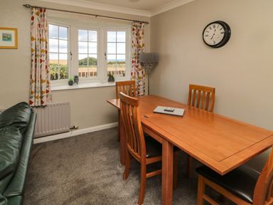 A dining area with wooden table and chairs near a window with patterned curtains at Island View Cottage in High Hauxley near Amble