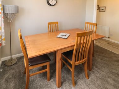 A dining area with a wooden table and four chairs a floor lamp and a wall clock at Island View Cottage in High Hauxley near Amble