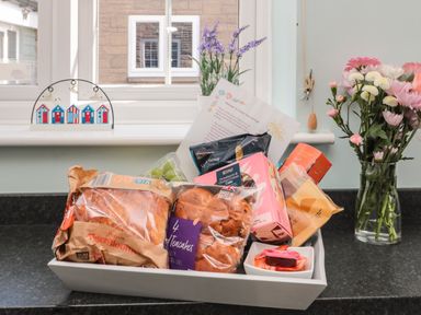 A kitchen windowsill with a welcome basket of food items and flowers in a vase at Island View Cottage High Hauxley near Amble