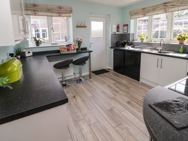 A kitchen with black countertops two black bar stools plants and flowers near windows at Island View Cottage in High Hauxley near Amble
