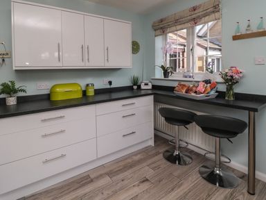 A kitchen with white cabinets black countertops two black bar stools flowers and a window at Island View Cottage in High Hauxley near Amble