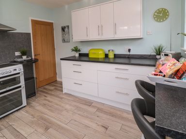 A kitchen with white cabinets black countertops a stove wooden door and various kitchen items at Island View Cottage in High Hauxley near Amble