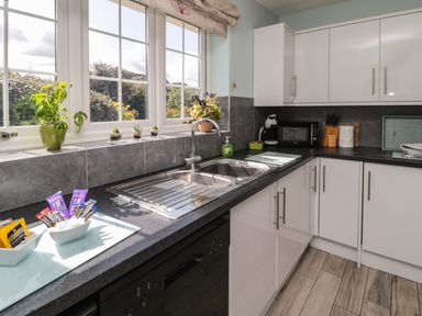 A kitchen with a sink dishwasher microwave and white cabinets at Island View Cottage in High Hauxley near Amble