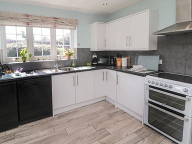 A kitchen with white cabinets a black countertop plants on the windowsill and a white oven at Island View Cottage in High Hauxley near Amble