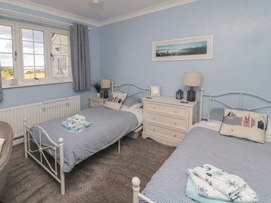 A bedroom with two single beds blue striped bedding a white chest of drawers and a window at Island View Cottage in High Hauxley near Amble