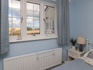 A bedroom with a window showing outdoor landscape blue patterned curtains a bedside table with a lamp and plant and a radiator below the window at Island View Cottage in High Hauxley near Amble