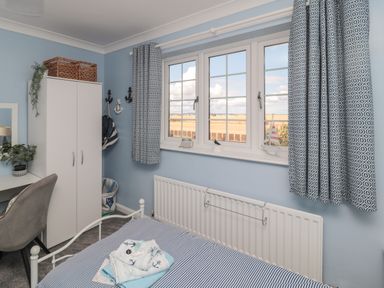 A bedroom with a bed a wardrobe a desk a chair and a window with patterned curtains at Island View Cottage in High Hauxley near Amble