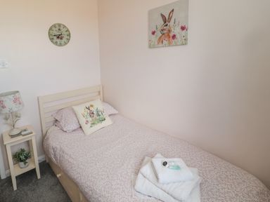 A small bedroom with a single bed a bedside table with a lamp a wall clock and a rabbit painting at Island View Cottage High Hauxley near Amble