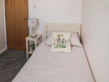 A bedroom with a single bed a bedside table and a wooden door at Island View Cottage in High Hauxley near Amble