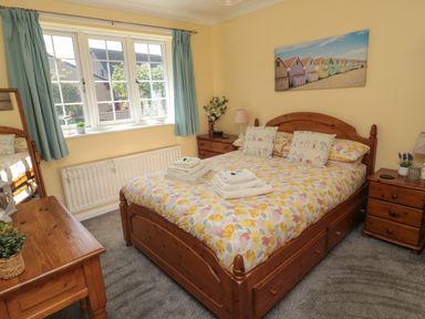 A bedroom with a wooden double bed with floral bedding two bedside cabinets a wooden dressing table and a window with blue curtains at Island View Cottage in High Hauxley near Amble