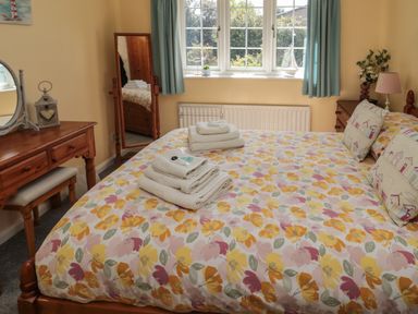 A bedroom with a bed with floral bedding and folded towels a dressing table and mirror at Island View Cottage in High Hauxley near Amble
