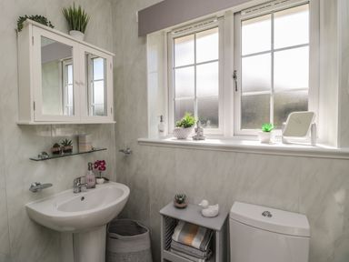 A bathroom with a sink, mirror cabinet, small shelf, window, toilet, and a small cabinet with towels at Island View Cottage in High Hauxley near Amble