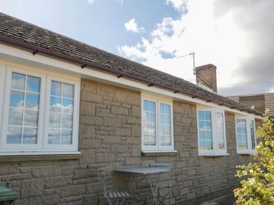 Exterior view of a stone house with four white windows a small table and two chairs outside Island View Cottage High Hauxley near Amble