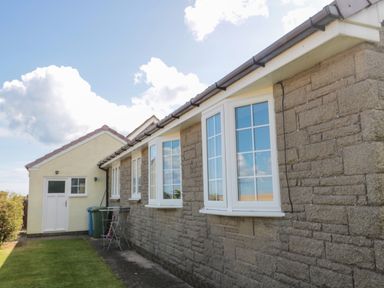 Exterior view of a building with stone walls and multiple white framed windows next to a yellow door at Island View Cottage in High Hauxley near Amble