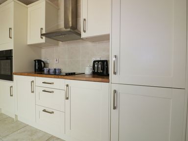A kitchen with white cabinets a stovetop black toaster black kettle and cups on the counter at Garden View Quintrell Downs near Newquay