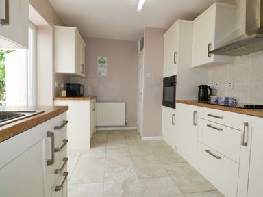 A kitchen with white cabinets wooden countertops and tiled floor at Garden View in Quintrell Downs near Newquay