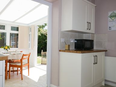 A kitchen corner with white cabinets a microwave on the counter and a dining area with a table and wooden chairs at Garden View in Quintrell Downs near Newquay