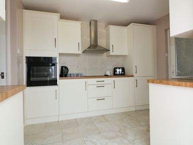 A kitchen with white cabinets a black oven black kettle black toaster and wooden countertops at Garden View in Quintrell Downs near Newquay