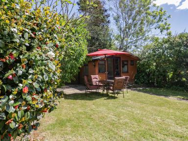 A garden with a wooden shed a table with four chairs and a red umbrella at Garden View Quintrell Downs near Newquay