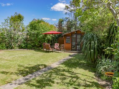 A garden with a wooden shed a table with chairs and a red umbrella at Garden View in Quintrell Downs near Newquay