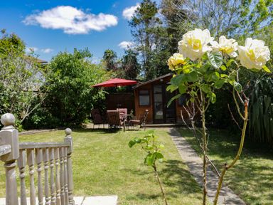 A garden with a lawn a small wooden shed a patio table with chairs and a red umbrella at Garden View in Quintrell Downs near Newquay