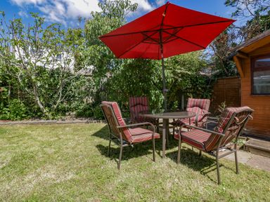 A garden with a table and four chairs under a red umbrella near a wooden shed at Garden View in Quintrell Downs near Newquay