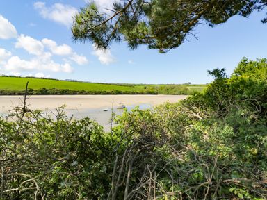 A view of a river with boats and green fields surrounded by bushes and trees at Garden View in Quintrell Downs near Newquay