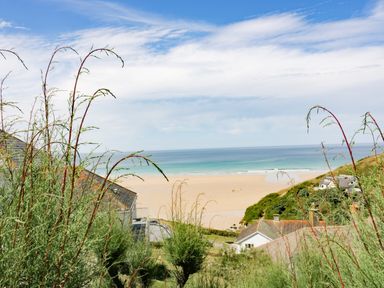 A view of a sandy beach and ocean with houses and greenery in the foreground at Garden View in Quintrell Downs near Newquay