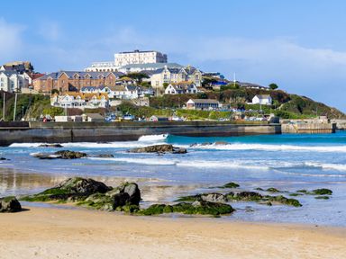 A beach with rocks and waves with houses and buildings on a hill in the background at Garden View Quintrell Downs near Newquay