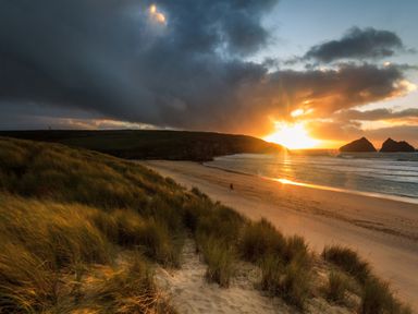 A sandy beach with grass-covered dunes and a sunset over the ocean at Garden View in Quintrell Downs near Newquay
