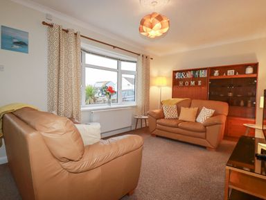 A living room with tan leather sofas and a wooden cabinet at Garden View in Quintrell Downs near Newquay