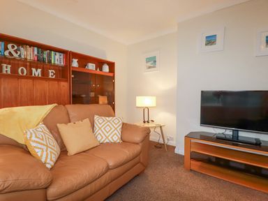 A living room with a brown sofa cushions wooden shelves a side table lamp and a television at Garden View in Quintrell Downs near Newquay