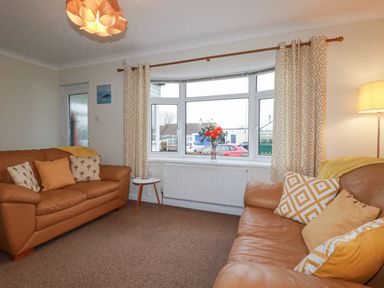 A living room with two brown sofas a small round table a window with patterned curtains and a floor lamp at Garden View in Quintrell Downs near Newquay