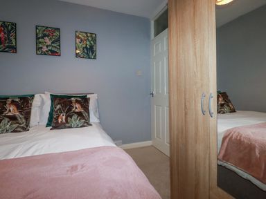 A bedroom with a bed with animal print pillows a wardrobe with mirrored door and framed pictures on the wall at Garden View in Quintrell Downs near Newquay