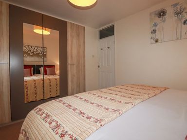 A bedroom with a bed covered by a patterned blanket a wardrobe with mirrored doors and a door on the wall at Garden View Quintrell Downs near Newquay