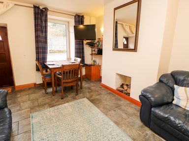 A living room with a dining table by a window a wall-mounted television and leather sofas at Hunter Cottage in Haltwhistle near Hadrians Wall