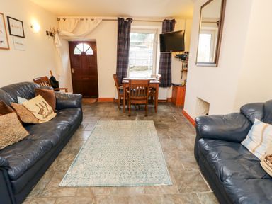 A living room with two leather sofas a dining table with chairs a wall-mounted television and a front door at Hunter Cottage in Haltwhistle near Hadrians Wall
