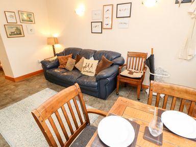 A living room with a blue sofa and cushions wooden chairs and a dining table with plates and glasses at Hunter Cottage in Haltwhistle near Hadrian's Wall