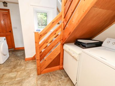 A laundry area with a washing machine and dishwasher under a wooden staircase next to a wooden door and window at Hunter Cottage in Haltwhistle near Hadrians Wall