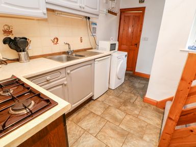 A kitchen with a gas stove sink cabinets a microwave fridge a washing machine and a wooden door at Hunter Cottage in Haltwhistle near Hadrians Wall