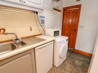 A kitchen area with a stainless steel sink a white microwave on top of a white washing machine and a wooden door at Hunter Cottage in Haltwhistle near Hadrian's Wall