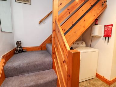 A carpeted staircase with wooden railing and a washing machine under the stairs at Hunter Cottage in Haltwhistle near Hadrians Wall