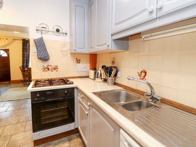 A kitchen with a gas stove oven a sink with dual basins kitchen utensils on the countertop and cabinets above at Hunter Cottage Haltwhistle near Hadrians Wall