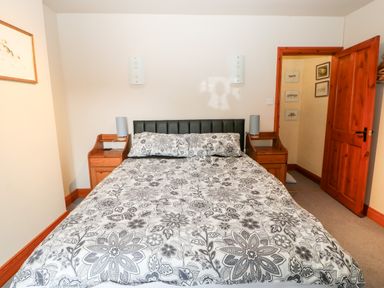 A bedroom with a double bed floral bedspread two wooden bedside tables with lamps and an open wooden door at Hunter Cottage in Haltwhistle near Hadrians Wall
