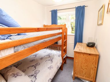 A small bedroom with a wooden bunk bed and a wooden cabinet with a radio on it and a window with blue curtains at Hunter Cottage in Haltwhistle near Hadrian's Wall