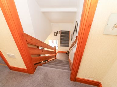 A carpeted staircase with wooden banisters and framed pictures on the walls at Hunter Cottage in Haltwhistle near Hadrians Wall