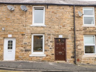 A stone building facade with three windows two satellite dishes two doors and a sloped sidewalk